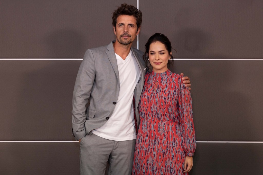 Danna García y un compañero posando juntos en una conferencia de prensa, sonriendo y con un fondo de colores neutros.