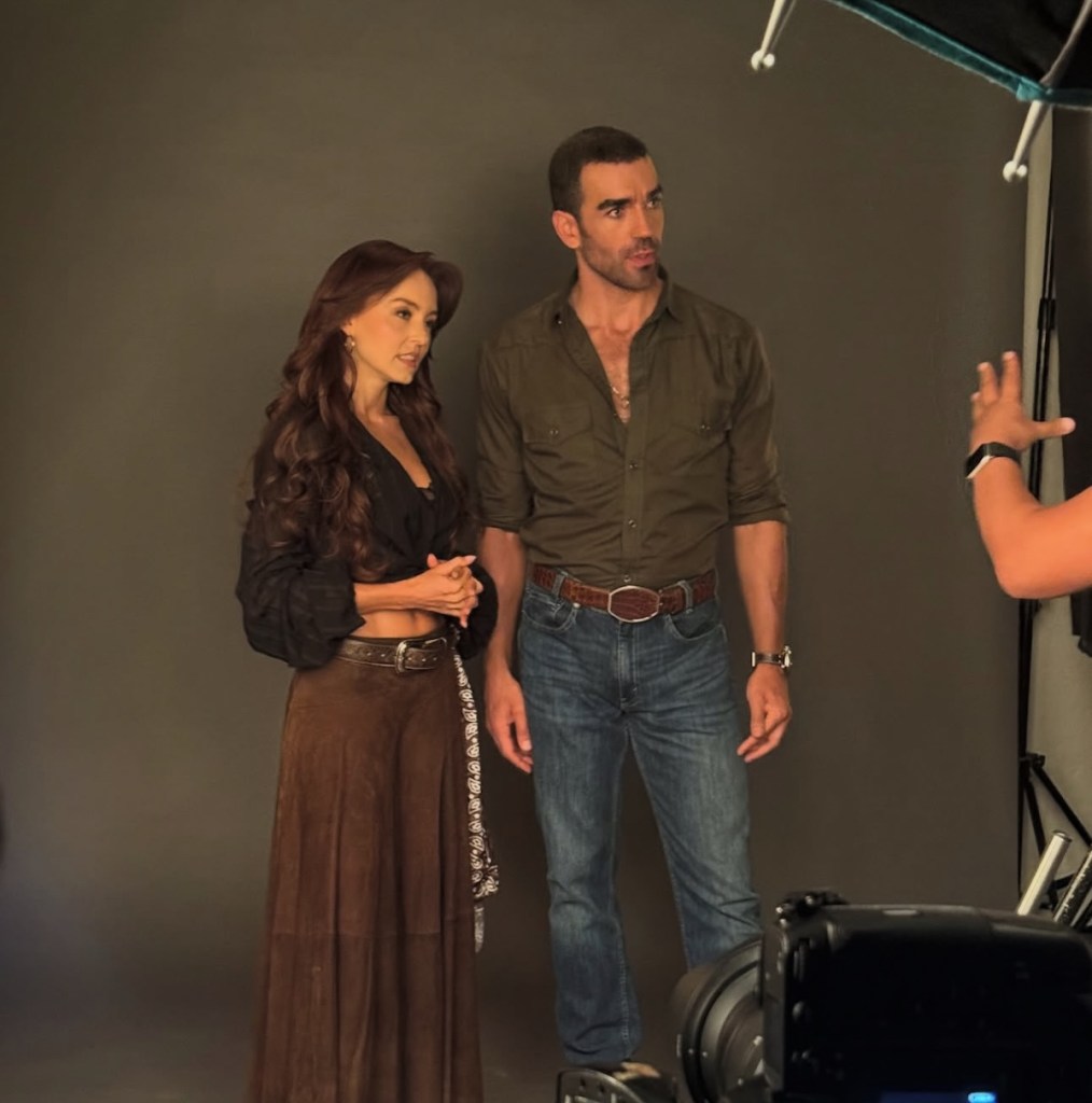 Angelique Boyer y un compañero de reparto posando para una sesión fotográfica, ambos vestidos con ropa casual y expresando atención hacia la cámara.