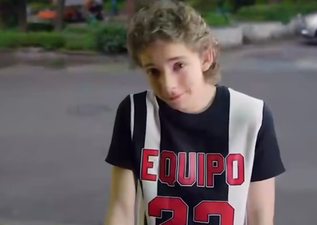 Un joven con camiseta de equipo en colores blanco y negro, haciendo una expresión despreocupada en un entorno urbano.