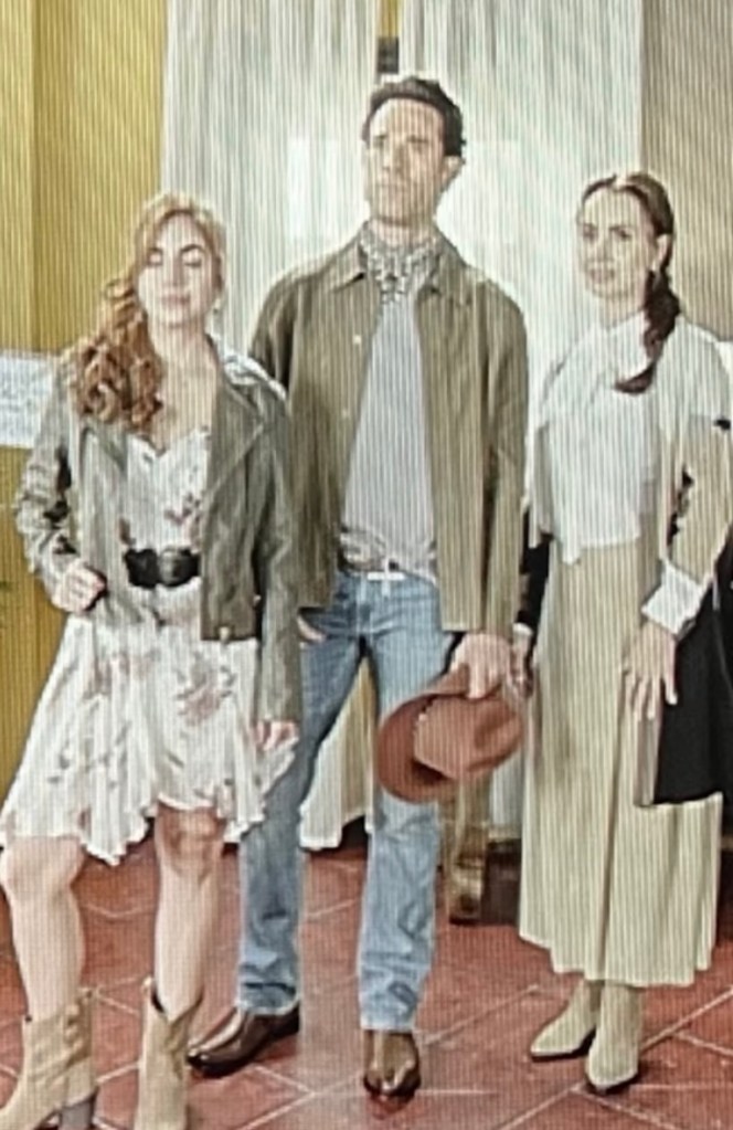Tres personajes de la telenovela 'Mi rival' posando frente a la cámara. La mujer a la izquierda lleva una chaqueta de cuero y vestido, el hombre en el centro viste un abrigo y jeans, y la mujer a la derecha lleva una blusa blanca y falda larga.