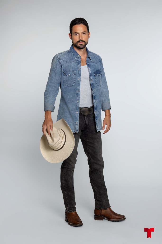 Hombre con camisa de mezclilla, camiseta gris y pantalones oscuros, sosteniendo un sombrero en la mano