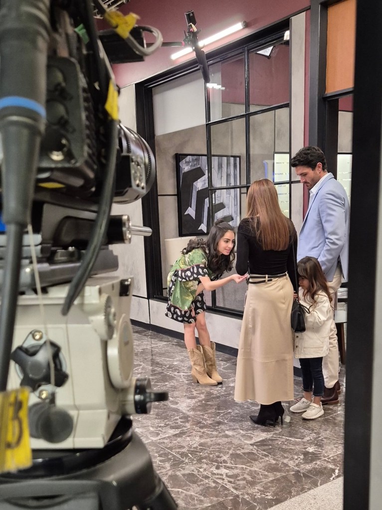Almudena López interactuando con otros actores en el set de grabación de la telenovela 'Regalo de amor'. Se observa un ambiente de trabajo colaborativo con cámaras y luces en el fondo.