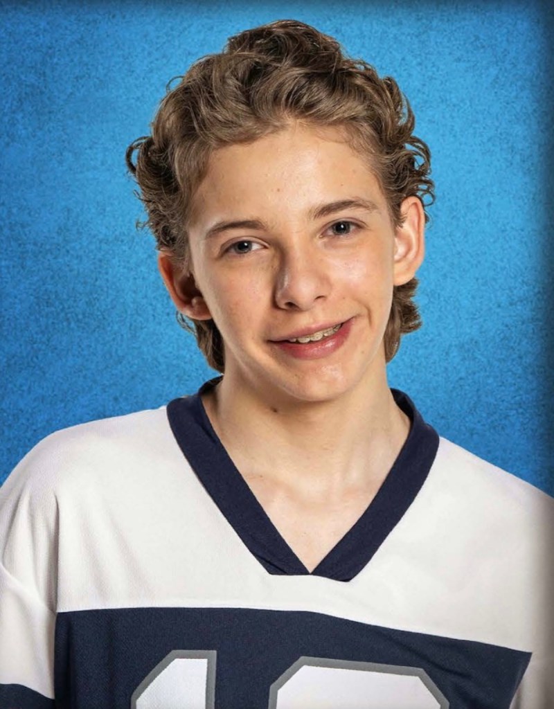 Retrato de un joven con cabello rizado y una sonrisa amigable, vestido con una camiseta deportiva de color blanco y azul, sobre un fondo azul.