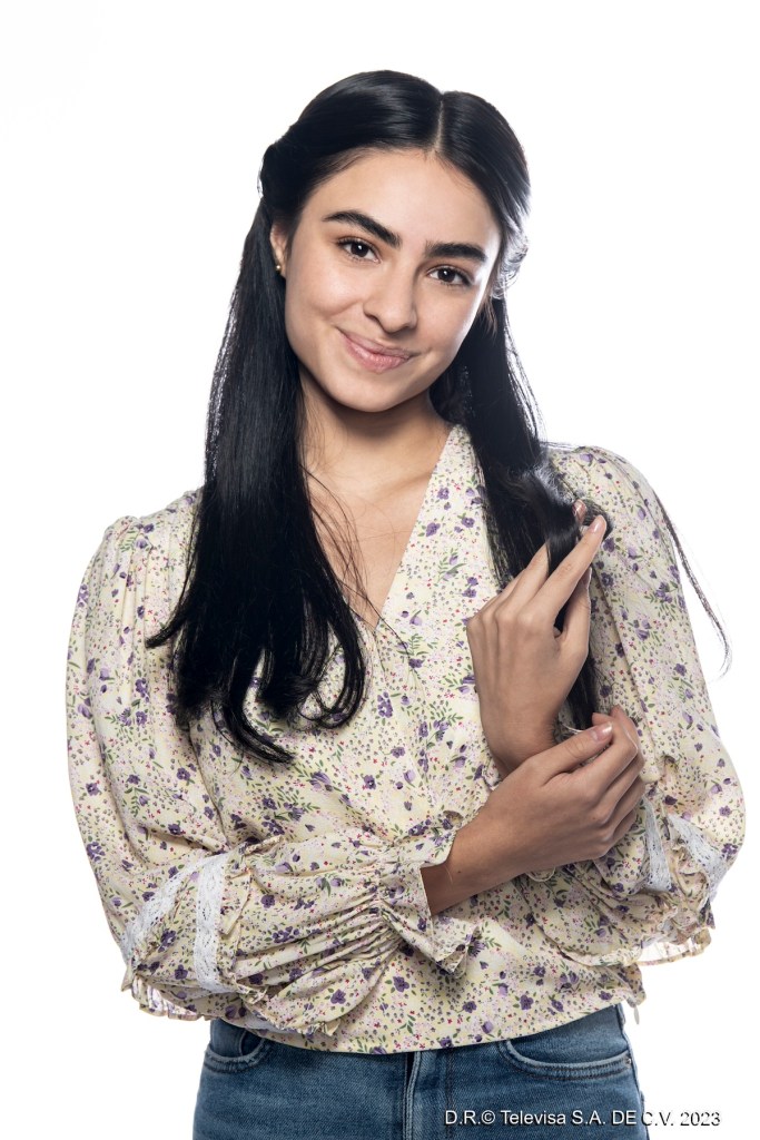 Retrato de Valentina Buzzurro sonriendo, vestida con una blusa de flores mientras sostiene su brazo con la mano, en un fondo blanco.