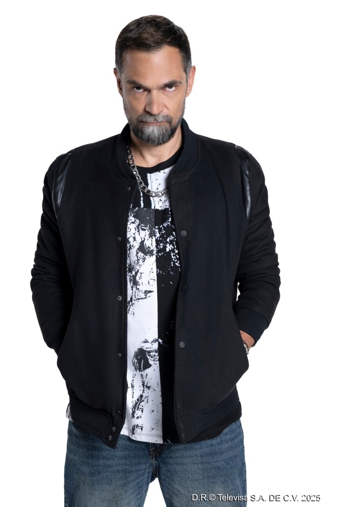 Retrato de un hombre con barba y cabello corto, vestido con chaqueta negra y camiseta blanca con diseño, posando con una expresión intensa.