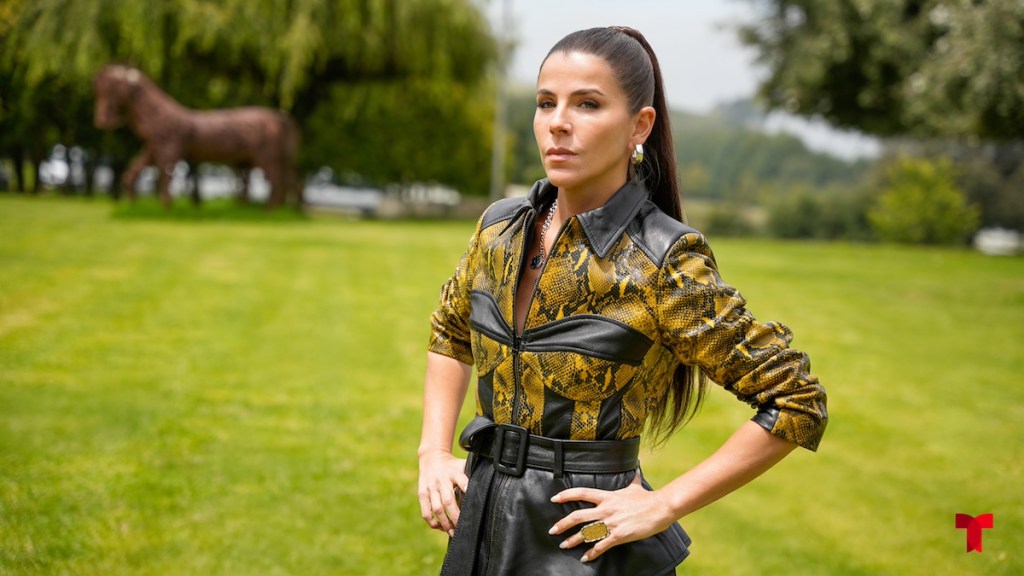 Mujer posando en un paisaje verde, vistiendo una camisa amarilla con patrones de serpiente y una falda negra de cuero.