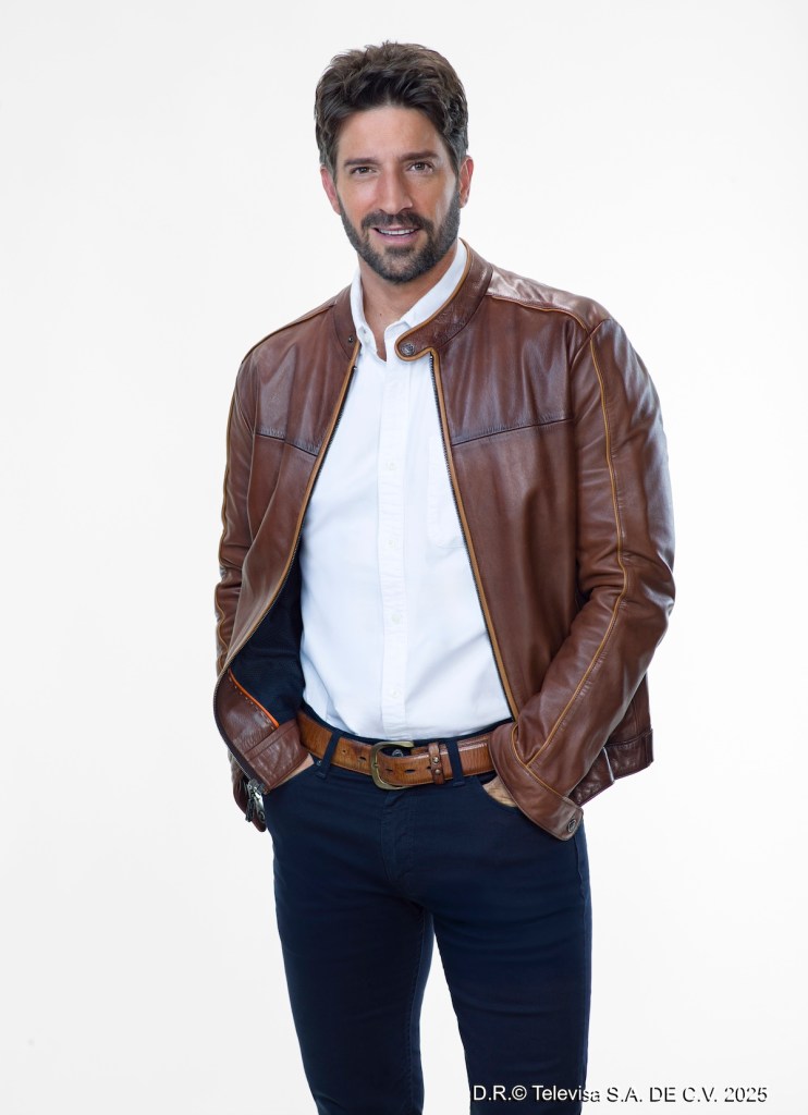 Actor posando con chaqueta de cuero marrón sobre una camisa blanca, con una sonrisa en un fondo blanco.
