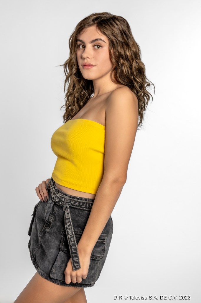Modelo femenina posando de perfil, vistiendo un top amarillo y una falda corta negra, con cabello ondulado y fondo blanco.