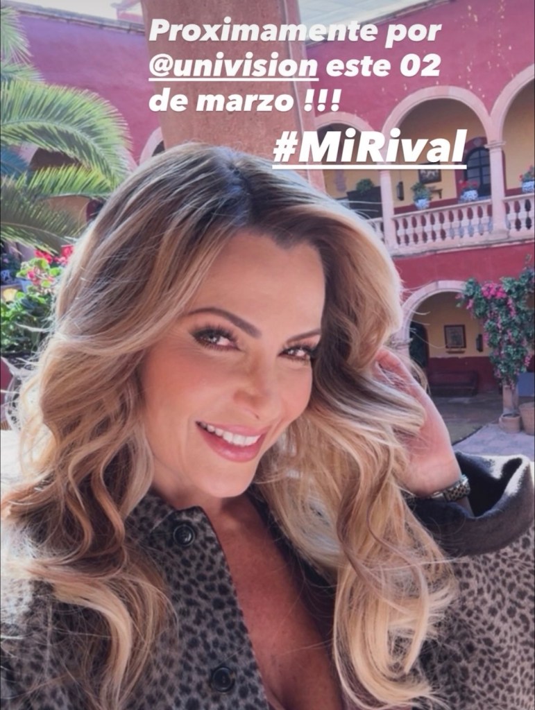 Retrato de una mujer sonriendo, con cabello ondulado y suelto, vestido con un abrigo de estampado de piel. El fondo muestra un patio colorido con plantas y arcos.