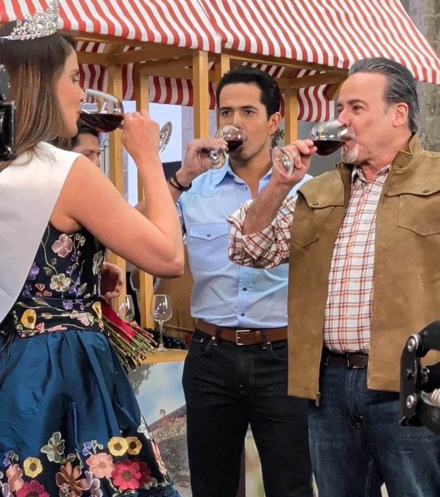 Tres personas levantando copas de vino en un ambiente festivo, con una mujer en un vestido decorado y una corona.