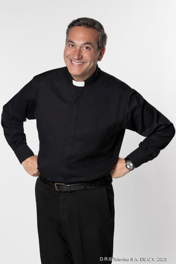 Hombre vestido de sacerdote con camisa negra y cuello blanco, sonriendo y con las manos en la cintura.