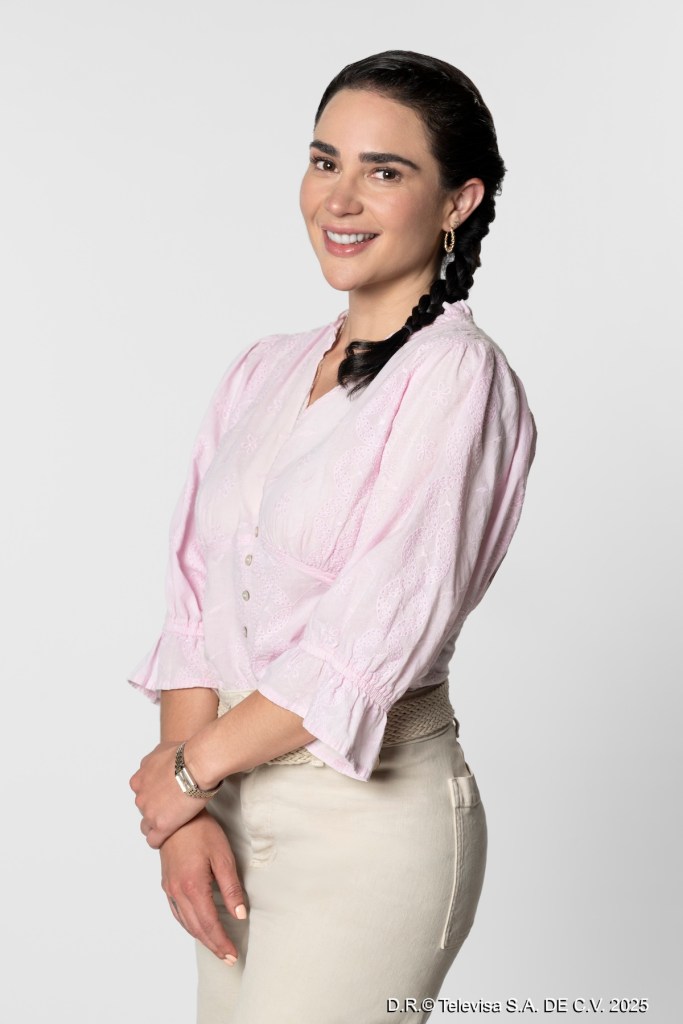 Mujer sonriente con blusa rosa y pantalones claros, con el cabello trenzado, posando en un fondo blanco.